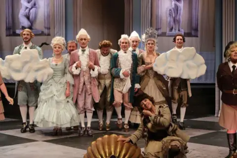 Piękna Lucynda w teatrze na 6. piętrze, w otoczeniu aktorów w strojach z epoki, przygotowuje się do spektaklu.