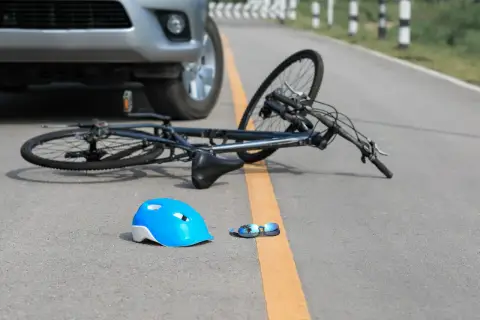 Samochód nie ustąpił pierwszeństwa rowerzyście. Na drodze leży przewrócony rower, niebieski kask i okulary.