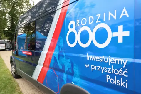 Niebieski bus z napisem "RODZINA 800+" i hasłem "Inwestujemy w przyszłość Polski". Obok rodziny, symbolizującej program 800 plus zmiany.
