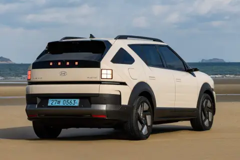 Kremowy Hyundai Nexo na plaży, z widokiem na morze i wyspę w oddali.