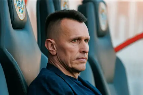Skupiony trener Zagłębia Lubin siedzi na ławce rezerwowych, analizując grę.