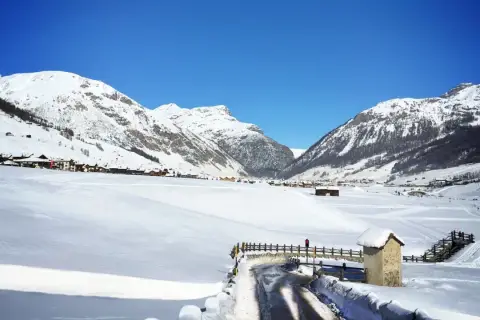 Paysage hivernal à Livigno, Italie. Montagnes enneigées, village pittoresque et route dégagée sous un ciel bleu éclatant.