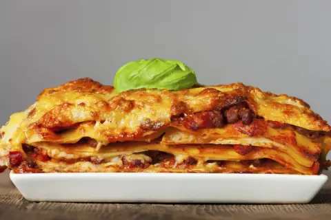 Una porción generosa de lasagna italiana, con capas de pasta, carne y queso derretido, coronada con una hoja de albahaca fresca.