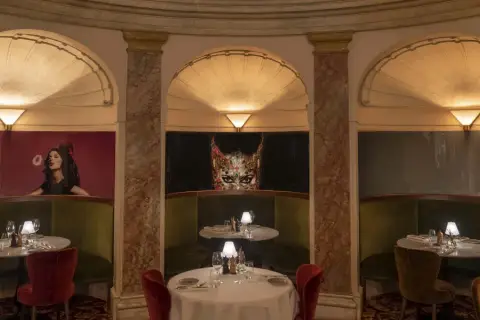 Elegant bås med gröna sammetssoffor och röda stolar. Konstverk av en kvinna och en mask pryder väggarna. Perfekt för en lyxig operan lunch.
