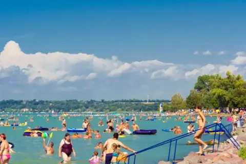 Tłumy ludzi kąpią się i relaksują nad wodą, szukając ochłody. Wszyscy zastanawiają się, gdzie nad Balaton, by cieszyć się słońcem i zabawą.