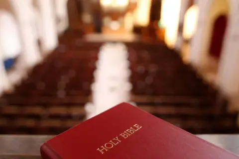 Czerwona Biblia leży na pierwszym planie, w tle widać rzędy pustych ławek w kościele, gdzie gromadzą się protestanci.