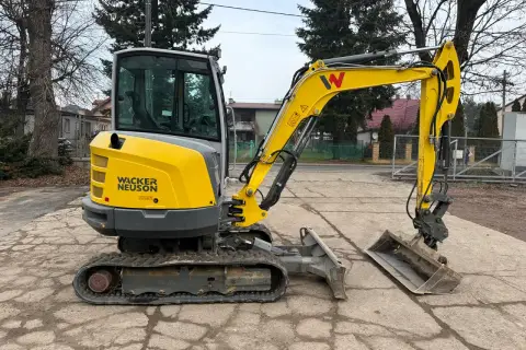 Żółta minikoparka Wacker Neuson z kabiną stoi na placu.