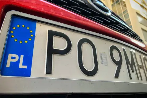Czerwony samochód z polską tablicą rejestracyjną PO 9MH0. Widoczny fragment grilla i logo marki.