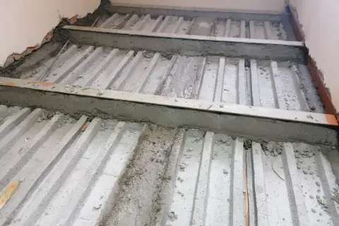 Prace nad tym, jak wzmocnić strop w starym domu. Widoczne betonowe belki i metalowe wsporniki, przygotowywane do dalszych prac budowlanych.