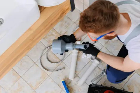 Instalator pracuje nad odpowietrzeniem kanału sanitarnego w domu parterowym, używając narzędzi do montażu rur.
