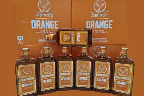 Jägermeister Orange, jeden z rodzajów Jägermeister, w butelkach i kartonach, z pomarańczowym motywem.