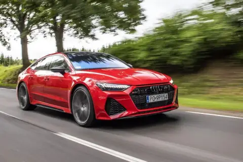 Czerwone Audi RS7 pędzi po drodze, otoczone zielenią drzew.