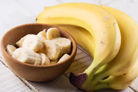 Dojrzały banan kcal w miseczce i pęczek bananów na drewnianym stole.