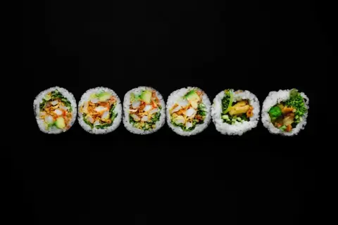 Sześć grubych rolek sushi futomaki z widocznym nadzieniem na czarnym tle.