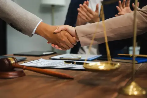 Uścisk dłoni prawników przy biurku z młotkiem sędziowskim i wagą sprawiedliwości. Zastanawiasz się, ile zarabia sędzia?