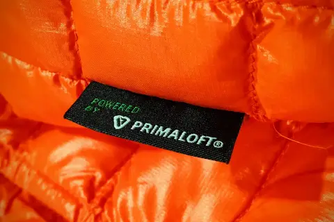 Pomarańczowa, pikowana tkanina z wszywką "Powered by Primaloft®". To materiał izolacyjny, który zapewnia ciepło.