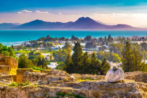 Tunis, afrykańska stolica nad Morzem Śródziemnym, rozciąga się od starożytnych ruin po białe domy, z górami w tle.