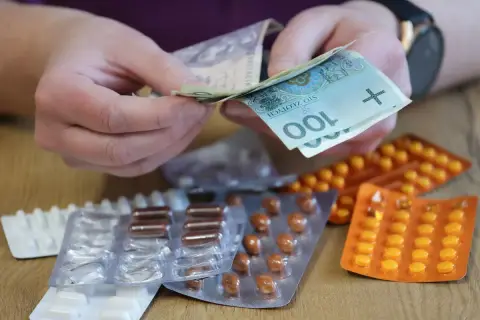 Dłonie liczą pieniądze nad lekami w blistrach. Możliwy zwrot za leki dla niepełnosprawnych.