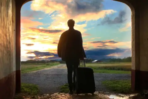Persona con maleta, lista para viajar, ante un atardecer espectacular. ¡Aprovecha las ofertas viajes última hora 2x1!
