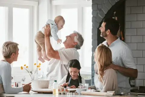 Radosna rodzina w kuchni. Dziadek podrzuca wnuka, babcia patrzy z uśmiechem. Dzieci pieką ciasteczka. To są prawdziwe babciowe dla kogo!