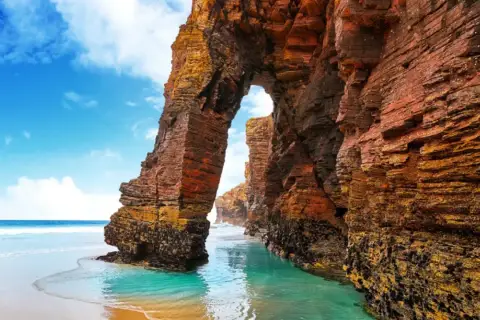 Arco natural en la playa de las Catedrales, un lugar ideal donde viajar en agosto en España.