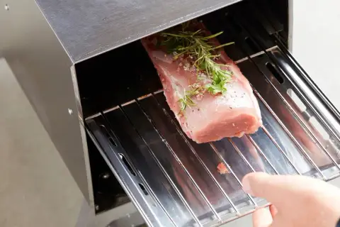 Un filet mignon fumé prêt à être cuisiné, assaisonné d'herbes et de poivre, est placé dans un fumoir. Une recette savoureuse en perspective.