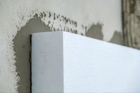 Biały styropian przyłożony do ściany z zaprawą. Czy to styrobeton czy styropian? Izolacja budynku.