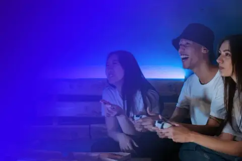 Trzech przyjaciół gra w gry wideo, śmiejąc się i jedząc pizzę. To świetna zabawa, jak na Steam!