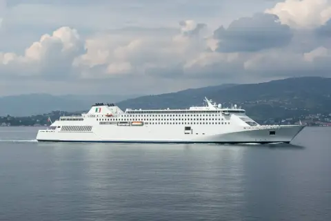 Traghetti per Ischia da dove partono? Questo grande traghetto bianco naviga in mare aperto, con montagne verdi sullo sfondo.