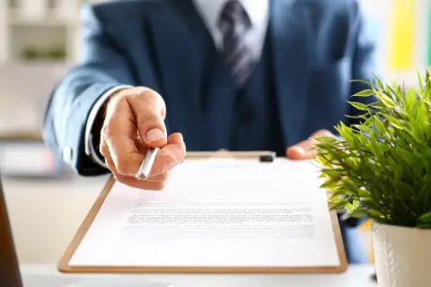Biznesmen podaje długopis do podpisania umowy, zgodnie z art. 52 Kodeksu pracy.