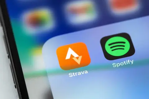 Ikona aplikacji Strava, idealna do śledzenia tras rowerowych, obok Spotify na ekranie smartfona.