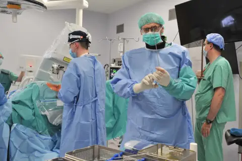 Chirurdzy w sterylnych strojach przygotowują się do skomplikowanej operacji kręgosłupa szyjnego. Czas jej trwania zależy od wielu czynników.
