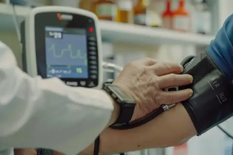 Lekarz mierzy ciśnienie pacjentowi. Na ekranie aparatu widoczny wynik ciśnienie 90/50.