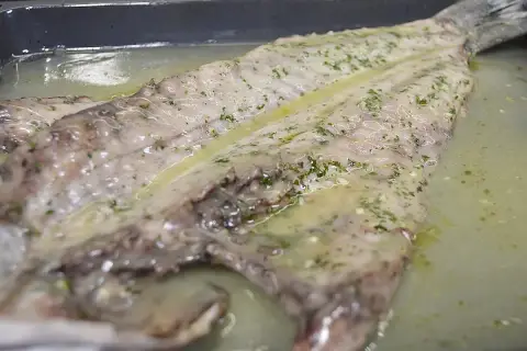Lubina salvaje preparada en una bandeja con salsa de limón y hierbas, lista para cocinar.