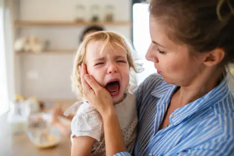 Mama próbuje uspokoić dwulatka, który przeżywa histerię. Dziecko głośno płacze, mama trzyma je czule.