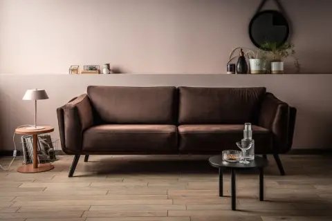 Elegancka kanapa w odcieniu barwy brązowej, obok stolik z lampką i dekoracjami.
