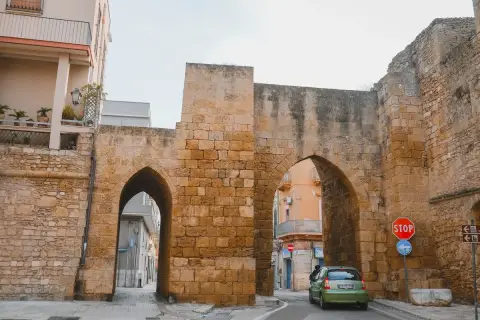 Antigua puerta de piedra con arcos, un coche verde pasa. Un lugar perfecto para un brindis por la historia.