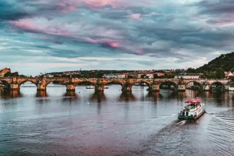 Zachód słońca nad Pragą, idealny na wycieczki jednodniowe z Jeleniej Góry. Widok na Most Karola i rzekę Wełtawę z łodzią.