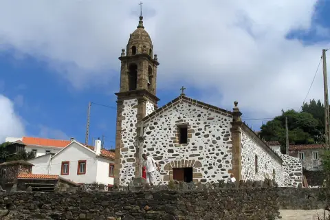 Iglesia de San Andrés de Teixido, con su campanario y fachada de piedra y cal, bajo un cielo nublado.