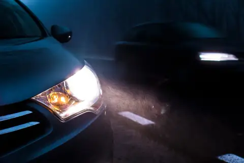 Mocna lampa led świeci jasno, rozświetlając mglistą noc i drogę. Inny samochód jedzie z przodu.