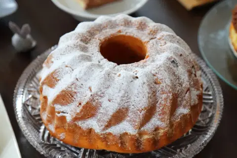 Puszysta babka drożdżowa, jak z babcinego przepisu, oprószona cukrem pudrem, na kryształowej paterze.