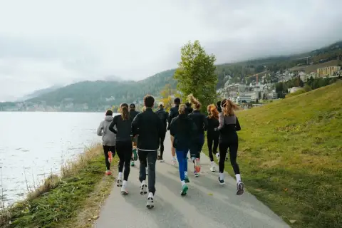 Grupa biegaczy w malowniczej scenerii nad jeziorem. Widok z tyłu na ludzi w sportowych strojach, którzy biegną ścieżką. To inspiracja, jak polubić bieganie.