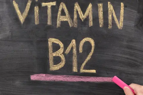 Kreidezeichnung "VITAMIN B12" auf einer Tafel, daneben eine Hand mit pinker Kreide.