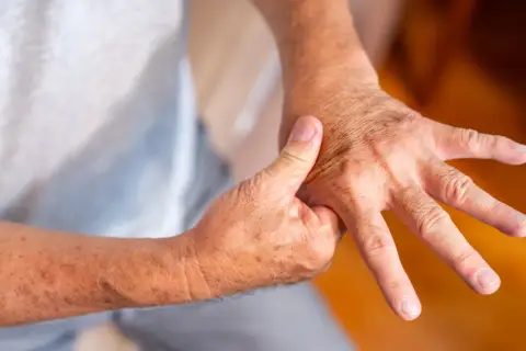 Osoba masuje dłoń, próbując złagodzić ból stawów w dłoniach.