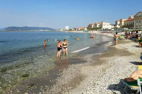 Plage de Massa, Italie. Des baigneurs profitent de l'eau claire et du soleil sur cette plage de galets animée.