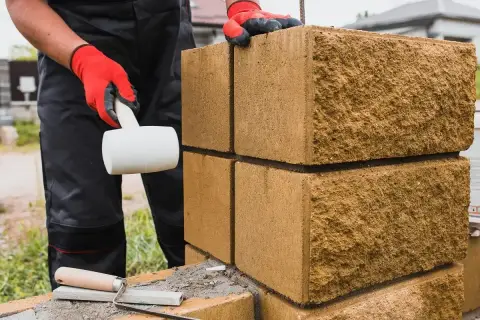 Budowa ogrodzenia z bloczków fundamentowych. Rękawice ochronne i gumowy młotek pomagają układać kolejne elementy.