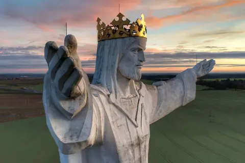 Majestatyczny pomnik Jezusa Chrystusa w złotej koronie, jeden z wielu pomników Jezusa w Polsce, wznosi się nad polami o zachodzie słońca.