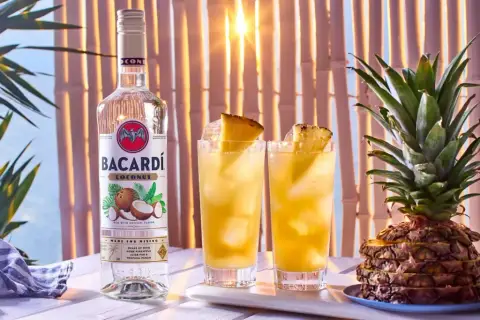 Butelka Bacardi Coconut obok dwóch drinków z ananasem i cała ananasowa piramidka. Idealne na tropikalne przyjęcie!