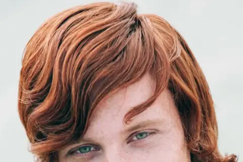 Ojos verdes y cabello pelirrojo ondulado, con pecas visibles en la piel.