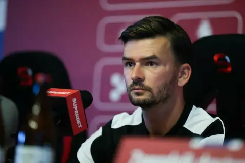 Trener Górnika Zabrze, w czarno-białej koszulce, siedzi przy mikrofonie Superbet.